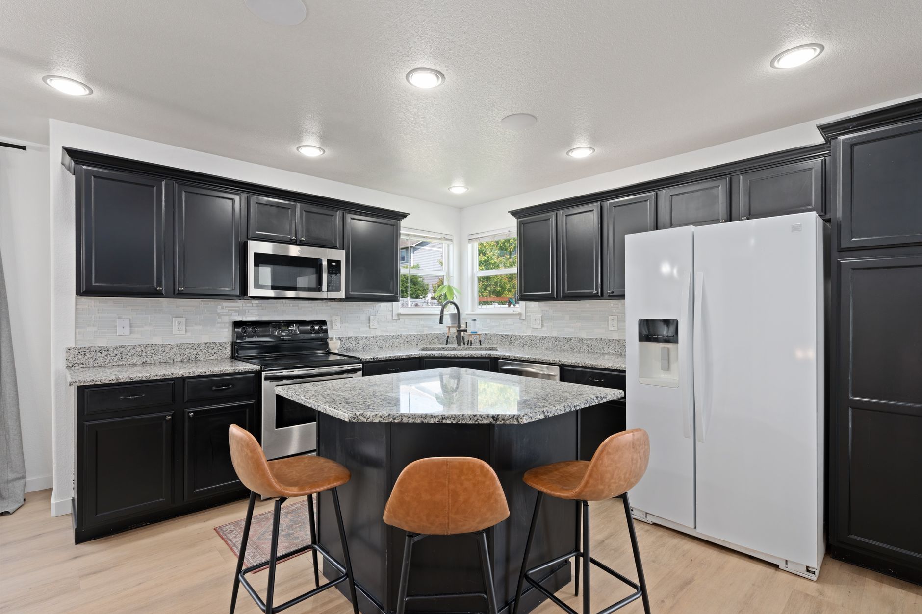 Spacious modern kitchen featuring black cabinets, granite countertops, and a white refrigerator in Redding, CA